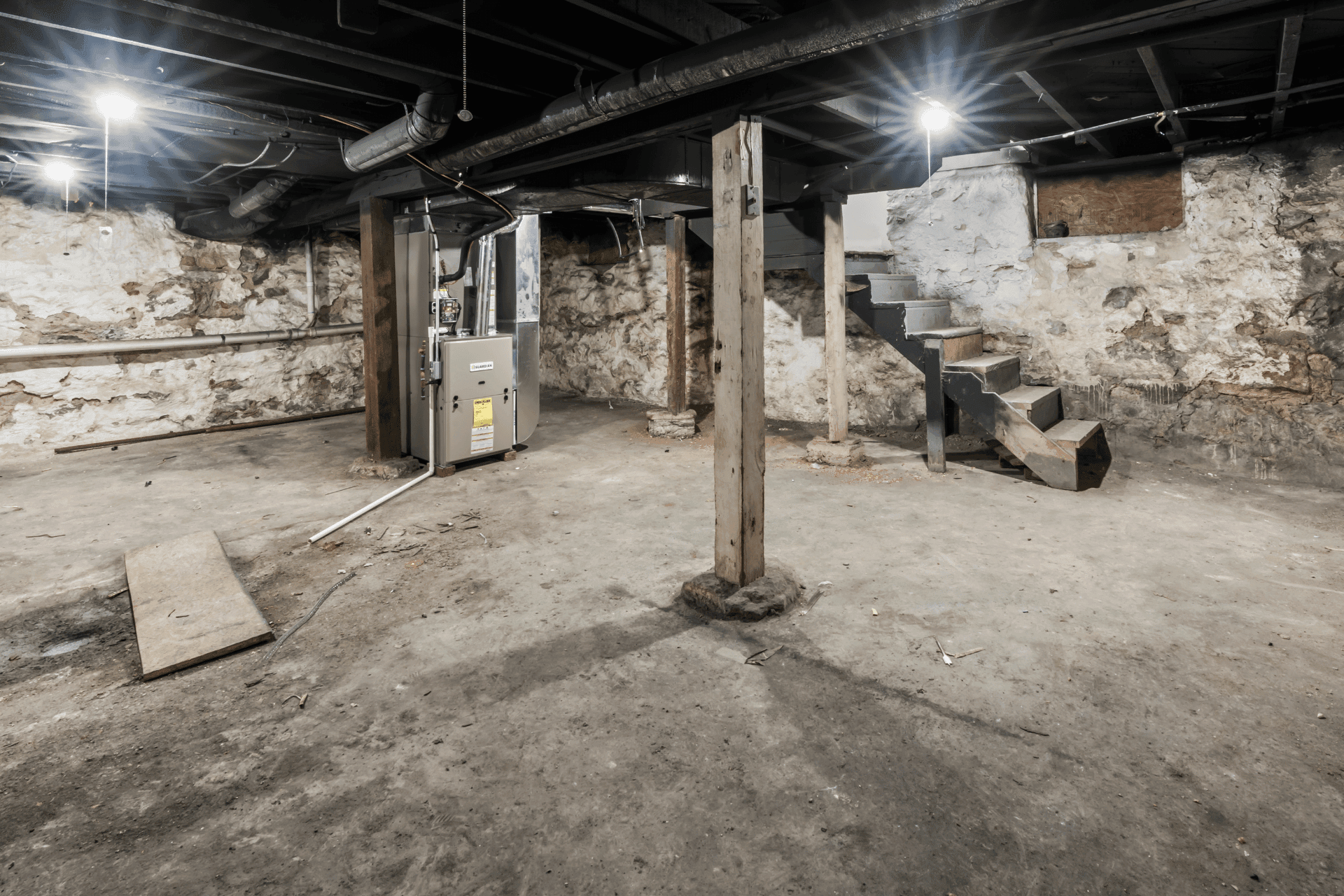 Basement with exposed stone walls, concrete floor, a furnace, and a metal staircase on the right.