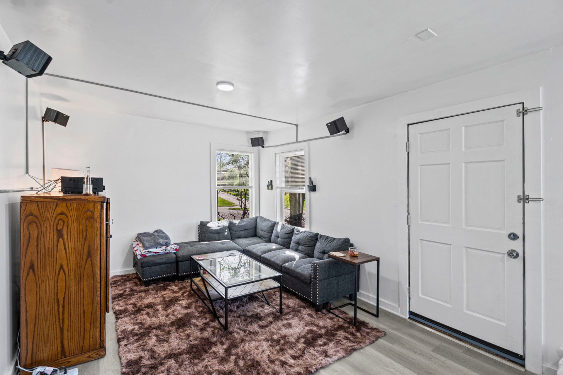 Cozy living room with a gray sectional on a brown shag rug, glass coffee table, and two windows letting in light.
