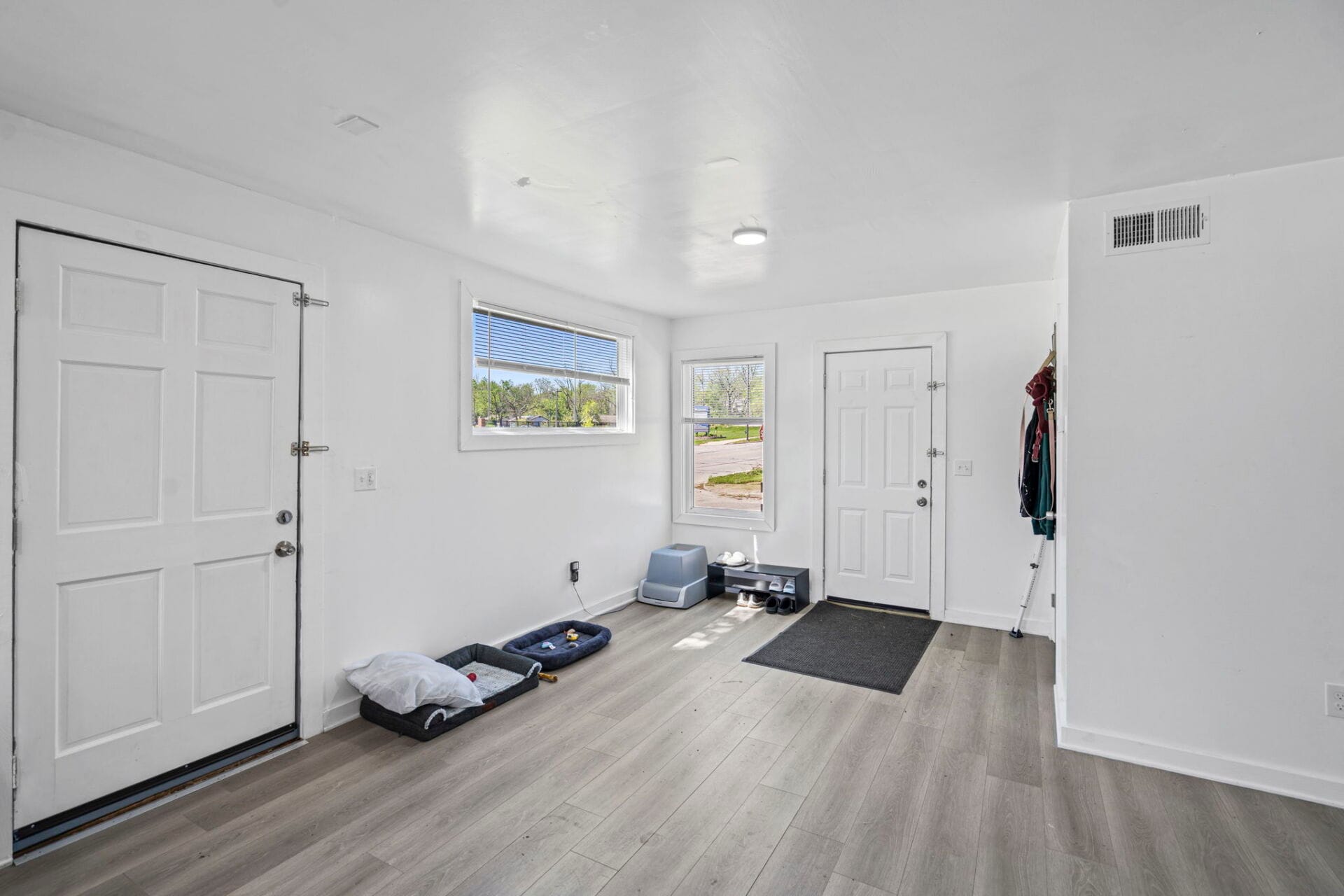 Bright white entry hall with a front door on the left, a window and door across, and small pet beds on the floor.