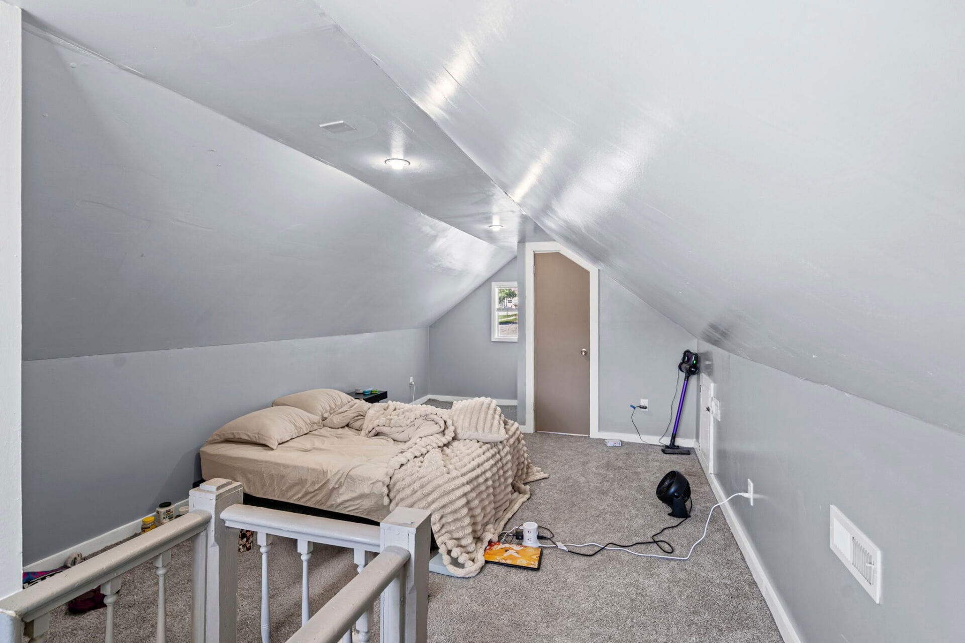 Cozy attic bedroom with a sloped ceiling, gray walls, a beige bed, and a chunky knit blanket.