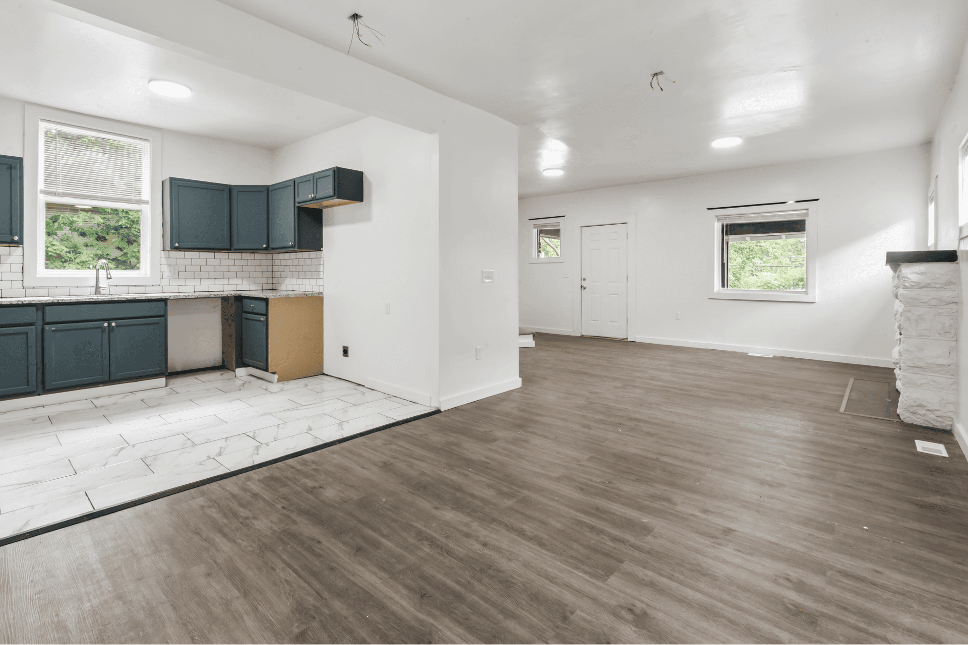 Open-plan kitchen and living space with blue cabinets, white subway tile backsplash, and wood-finish flooring throughout.